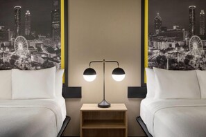 Habitación de hotel con dos camas blancas, una mesita de noche con lámpara y un papel tapiz con vista a la ciudad.