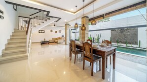 A modern interior with a dining area, staircase, and a pool view. - Q LE Villas (Seminyak)