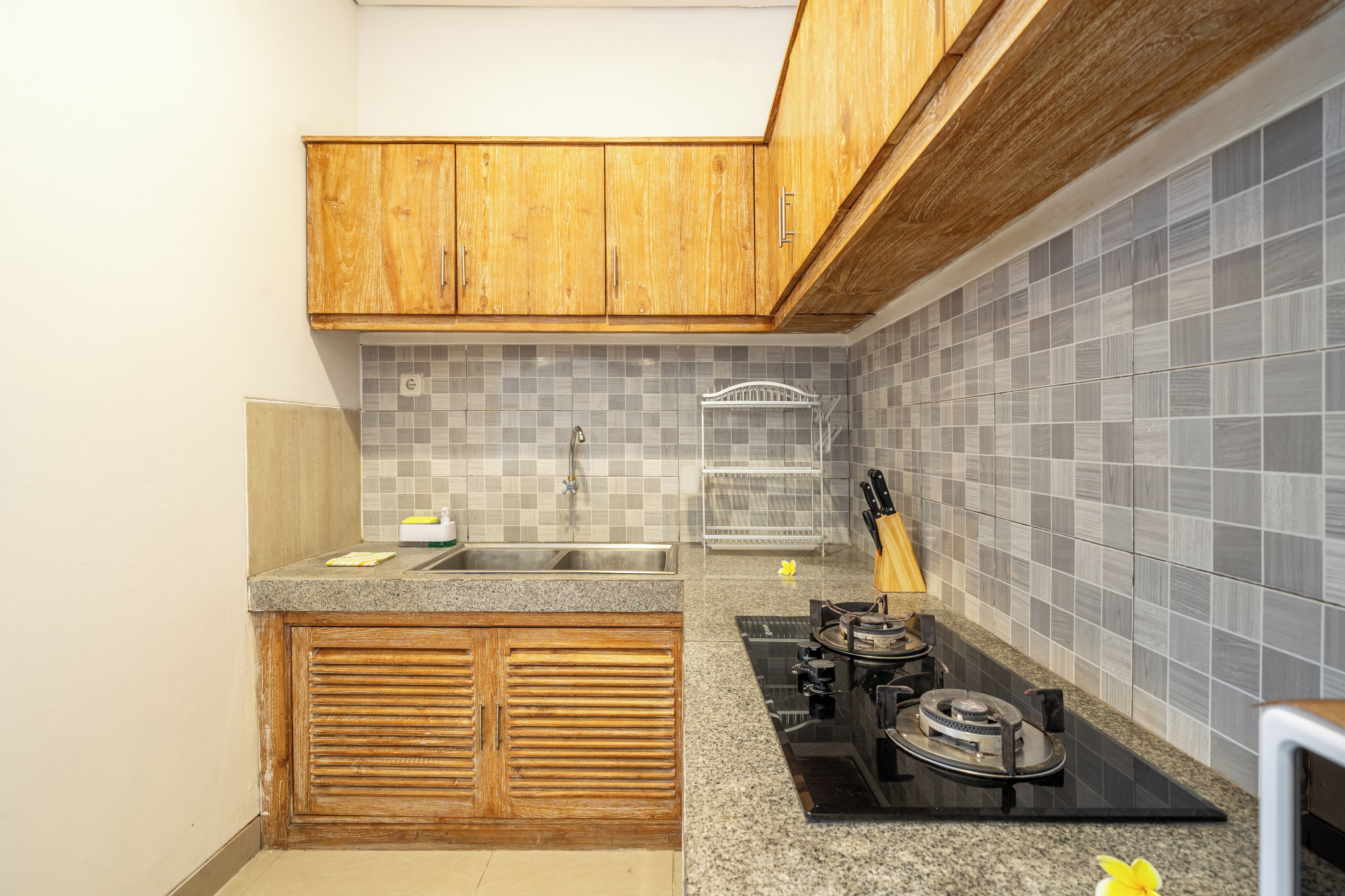 Una cocina con armarios de madera, salpicadero de azulejos, pileta de acero inoxidable, cocina a gas y bloque de cuchillos.