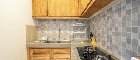 Una cocina con armarios de madera, salpicadero de azulejos, pileta de acero inoxidable, cocina a gas y bloque de cuchillos.