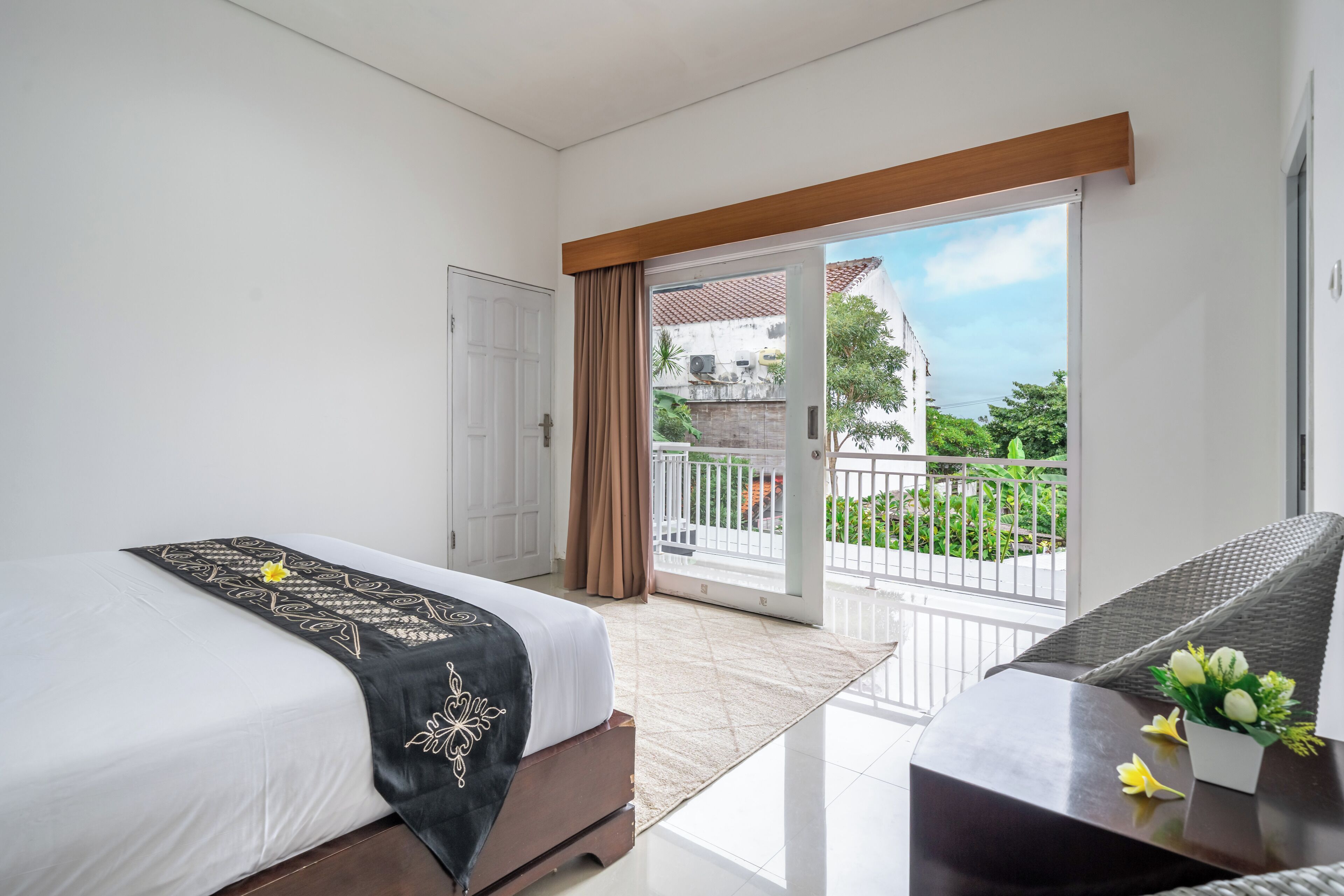 Ein Hotelzimmer mit Bett, Sofa und Balkon mit Blick auf Grünflächen und Gebäude.