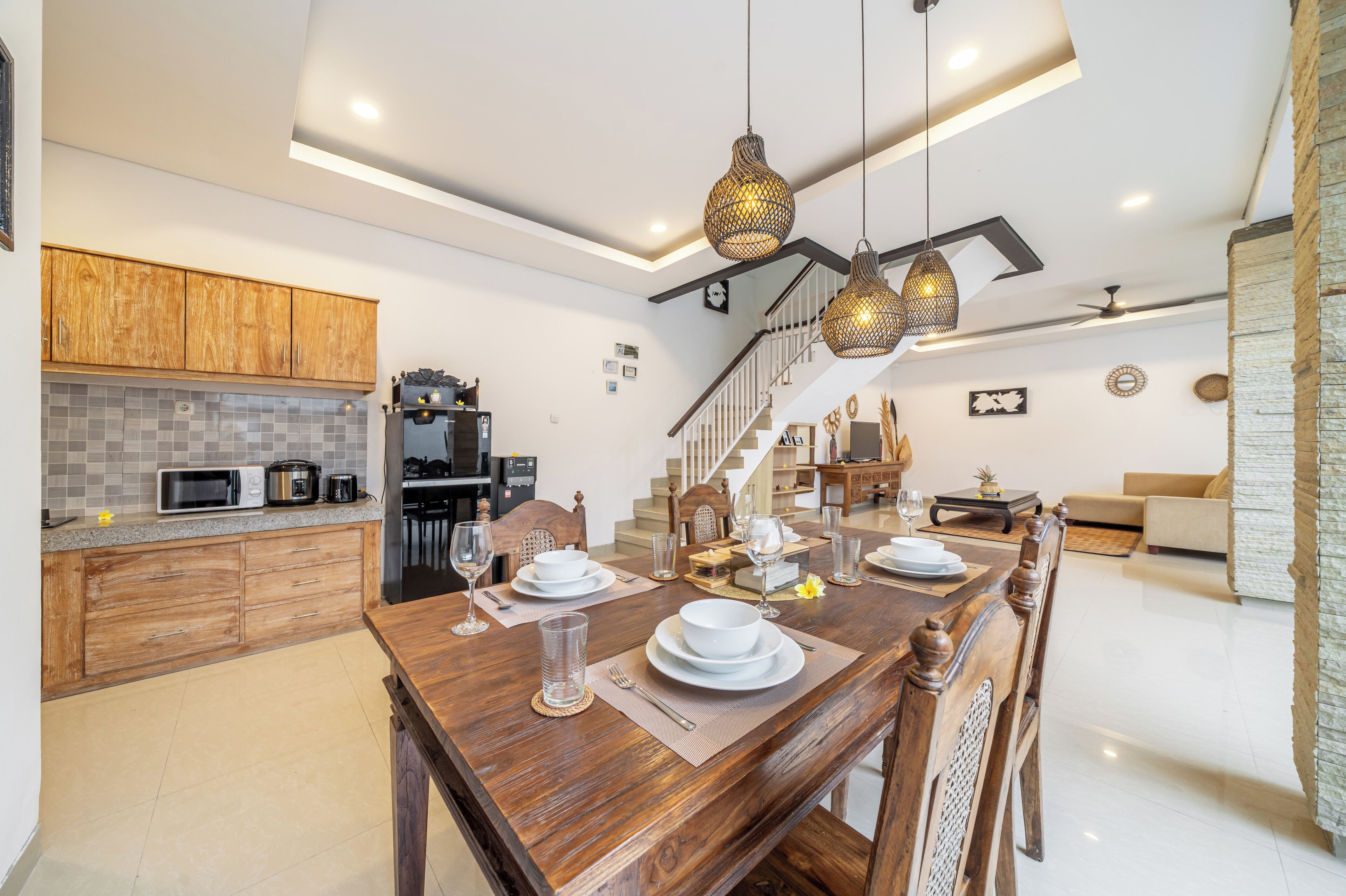 A modern kitchen with wooden cabinets, a dining area with a wooden table set for four, and a staircase leading to a loft bedroom.