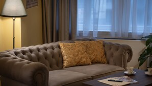 A brown sofa with a patterned cushion, a lamp, a remote control, and a magazine on a wooden table. - Deluxe 1‑BR Apartment Sleeps 3– Historic Palace, Heart of Prague (Prague)