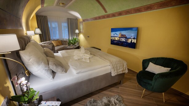 A hotel room with a bed, a green armchair, a lamp, a plant, and a painting on the wall. - Deluxe 1‑BR Apartment Sleeps 3– Historic Palace, Heart of Prague (Prague)