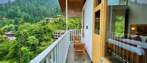 A balcony with a view of a forested hillside, a wooden table, and a bed with a view.