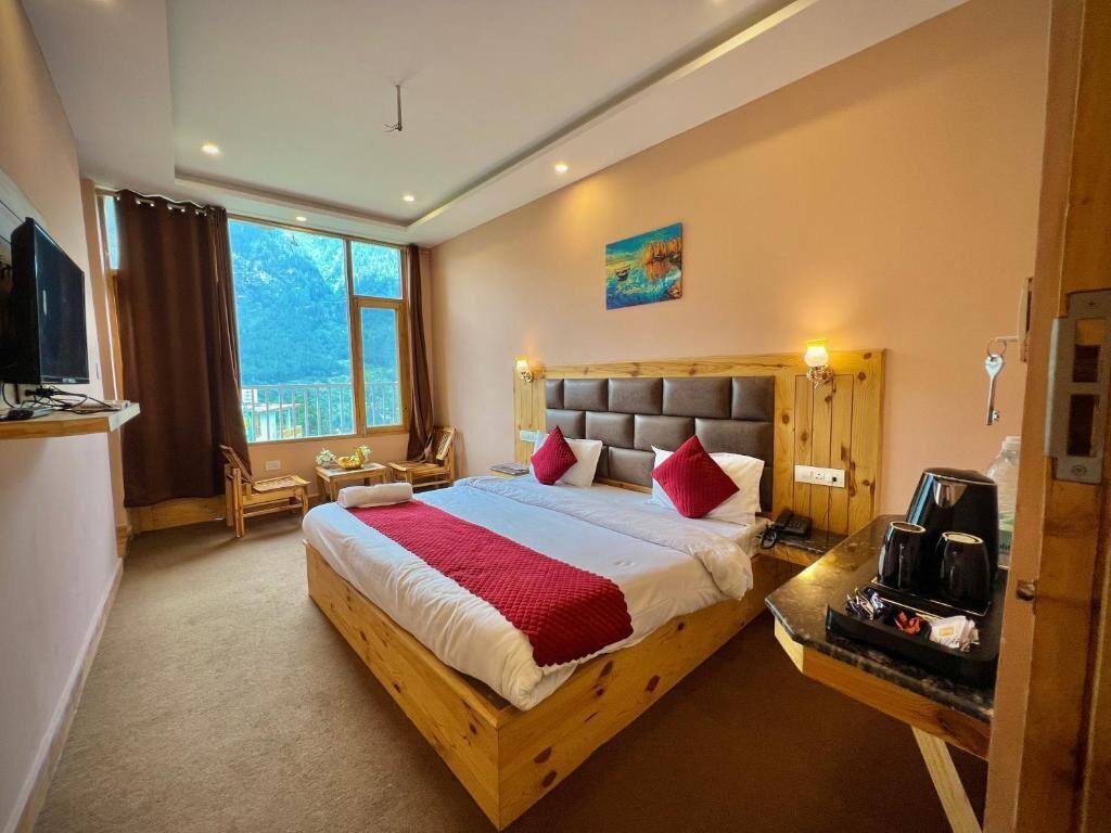Une chambre à coucher avec un lit en bois, une télévision, un bureau avec une machine à café et une fenêtre avec des rideaux.