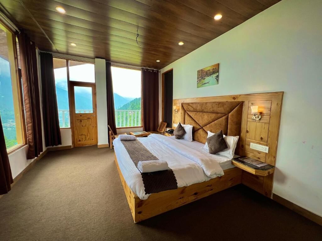 A wooden-framed bed with a view of mountains through a balcony door.