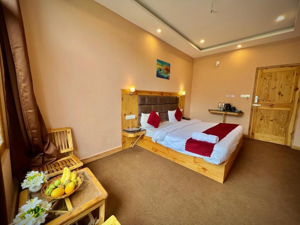 Un dormitorio con cama de madera, una mesita de noche, una pequeña mesa con frutas y flores, y un armario de madera.