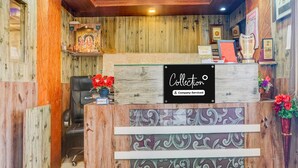 A reception desk with a 'Collection' sign, wooden paneling, a black office chair, and decorative flowers. - Collection O Mahabaleshwar (Jaoli)