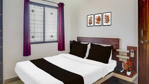 A hotel room with a bed, an air conditioner, a window with purple curtains, and three framed pictures on the wall. - Collection O Mahabaleshwar (Jaoli)