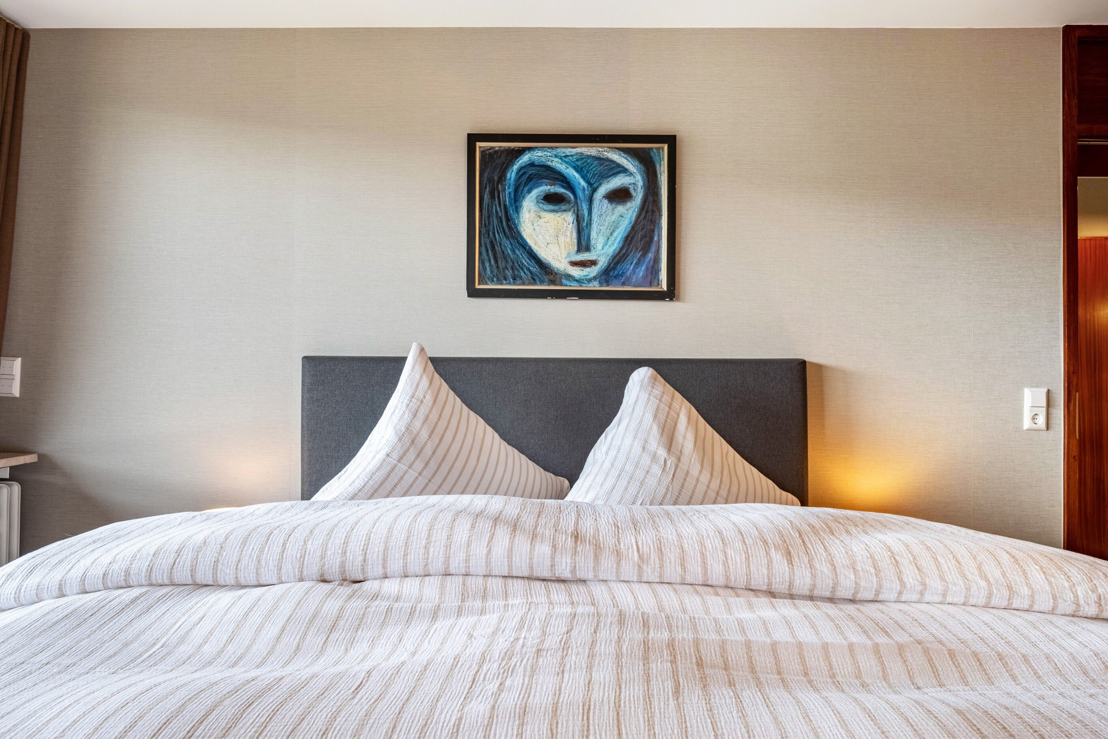 Une chambre d’hôtel avec un lit, une tête de lit, un tableau au mur et une table de chevet.