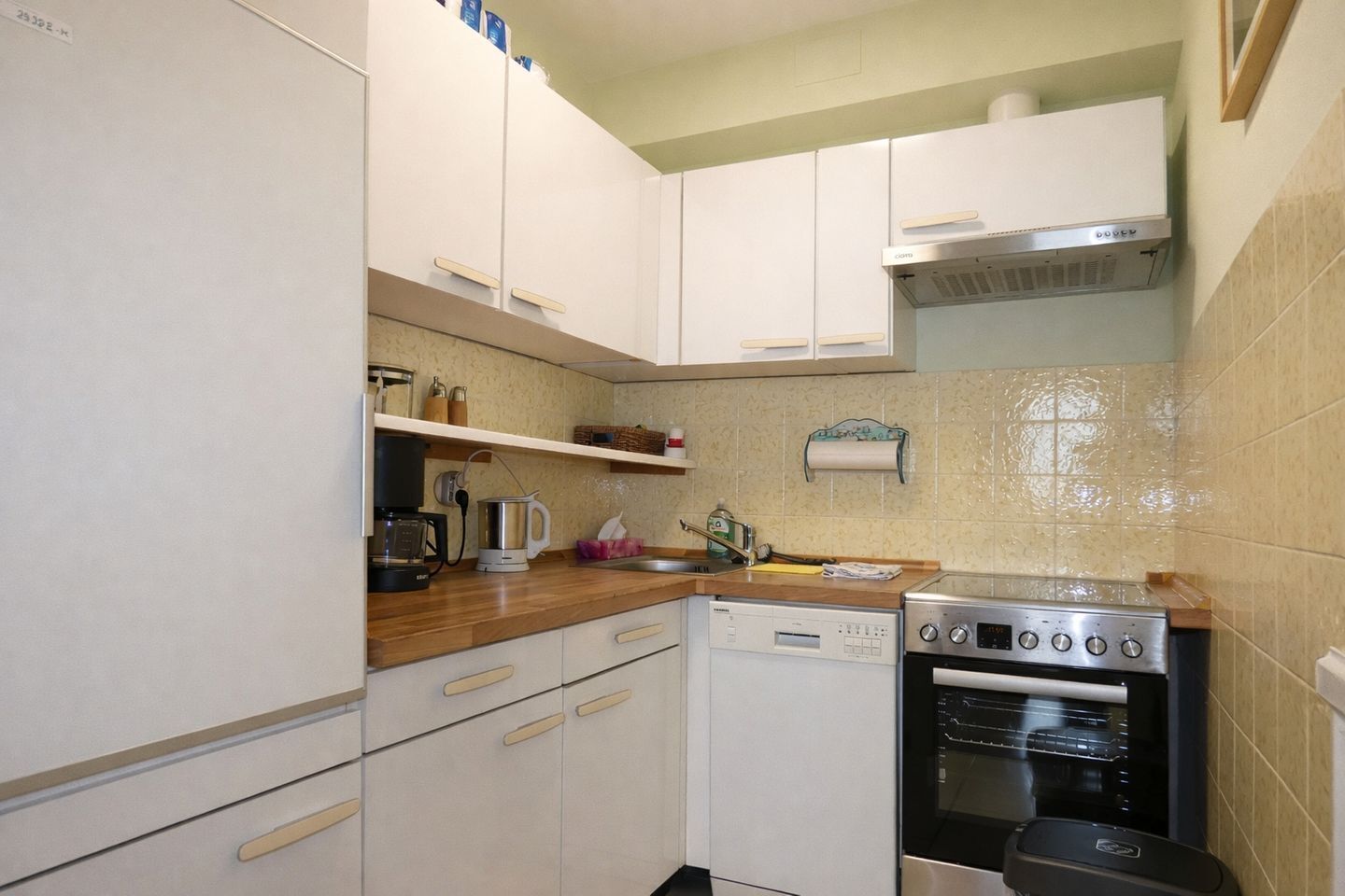 Eine kleine Küche mit weißen Schränken, einer Kaffeemaschine, einem Toaster und einem Herd.