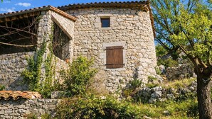 A stone building with a tiled roof, a small window with wooden shutters, and a stone wall with vegetation around it. - In Balazuc, terrace overlooking the Ardèche gorges, 300 m from the beach. (Balazuc)