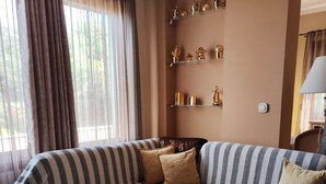A modern living room with a sectional sofa, a glass coffee table, and decorative items on shelves. - Gavrilis apartments: Deluxe One-Bedroom Apartment (Nenita)
