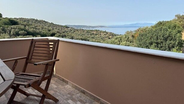 A balcony with a view of a coastal landscape, a wooden chair, and a table. - Gavrilis apartments: Deluxe One-Bedroom Apartment (Nenita)