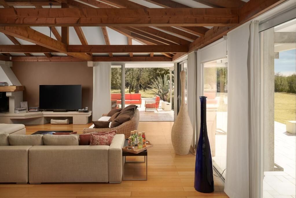 Una sala moderna con techo de madera, televisor de pantalla plana, sofá color beige y un amplio ventanal con vistas al exterior.