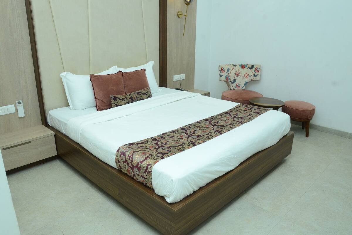A neatly made bed with a patterned bedspread, a wooden headboard, and a small round table with a chair beside it.
