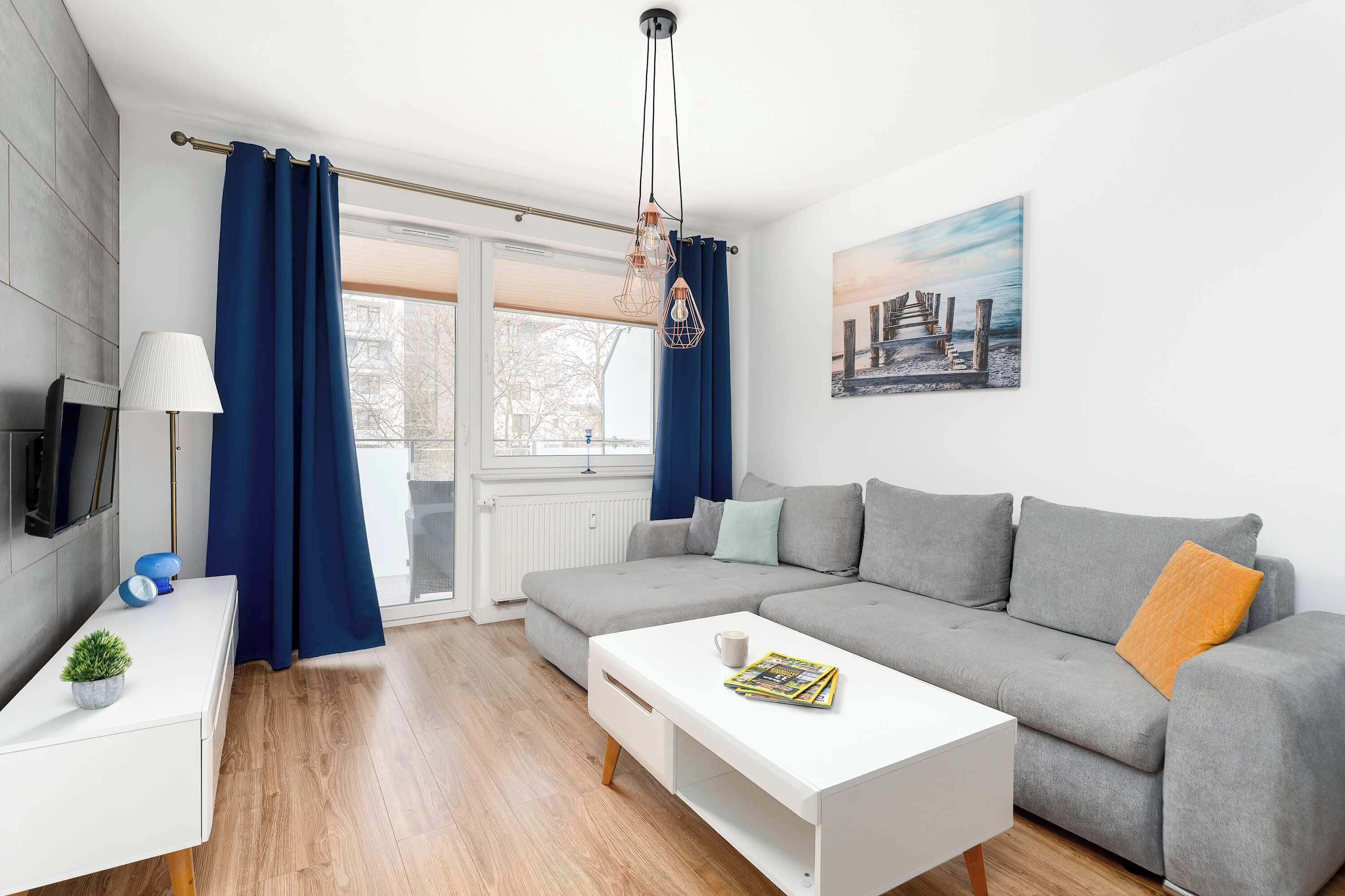 A modern living room with a grey sofa, white coffee table, and a blue curtain.