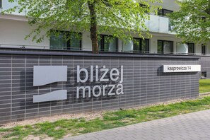 A building with a sign reading "blizej morza" and "kasprowicz 14". - Seaside Apartment | Balcony, Gym, 1 km to the Beach (Kołobrzeg)