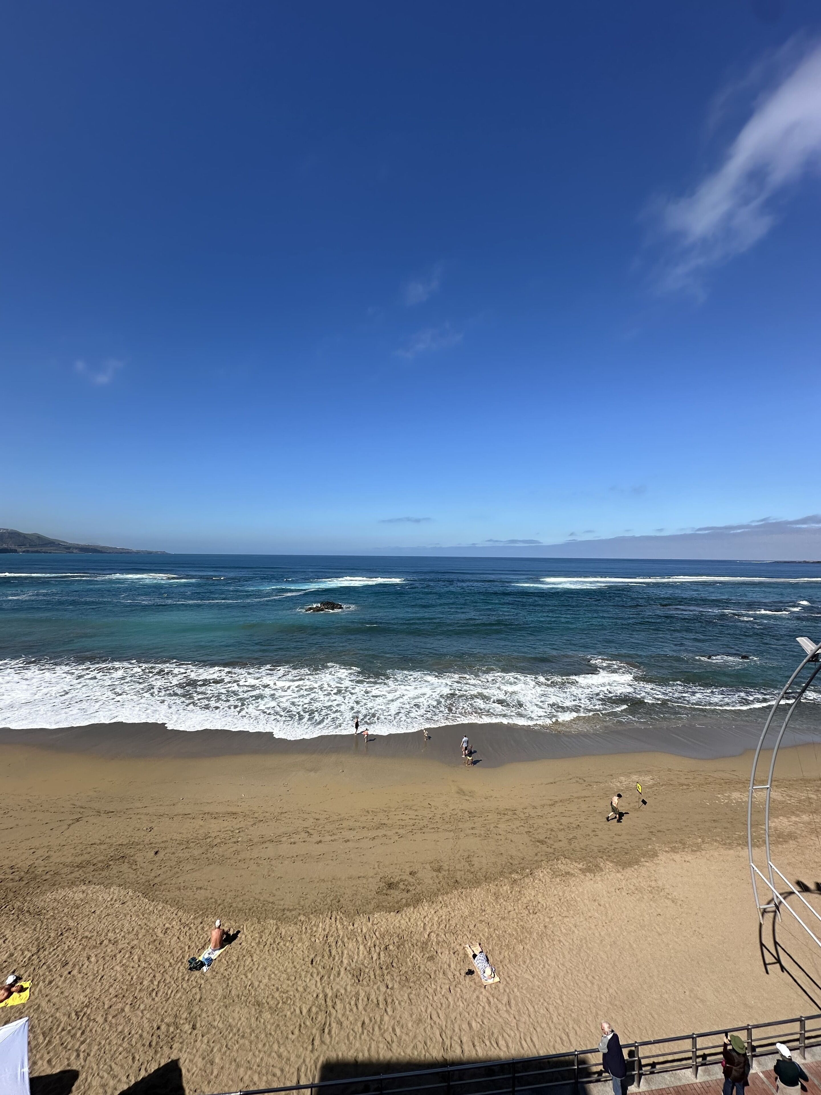 A beach with waves, people, and a clear sky.