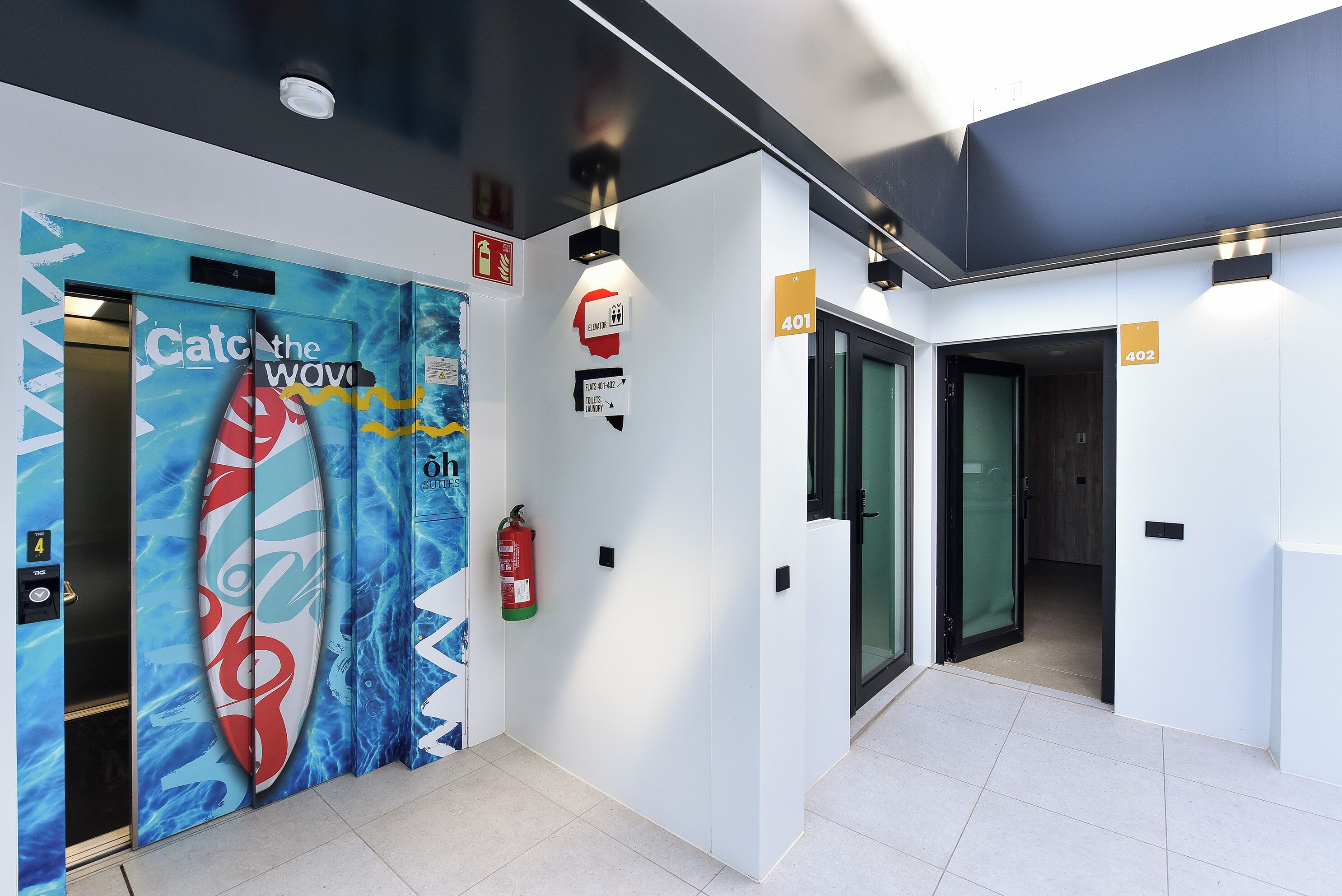 A modern interior with a blue and white color scheme, an elevator with a surfboard design, and numbered doors.