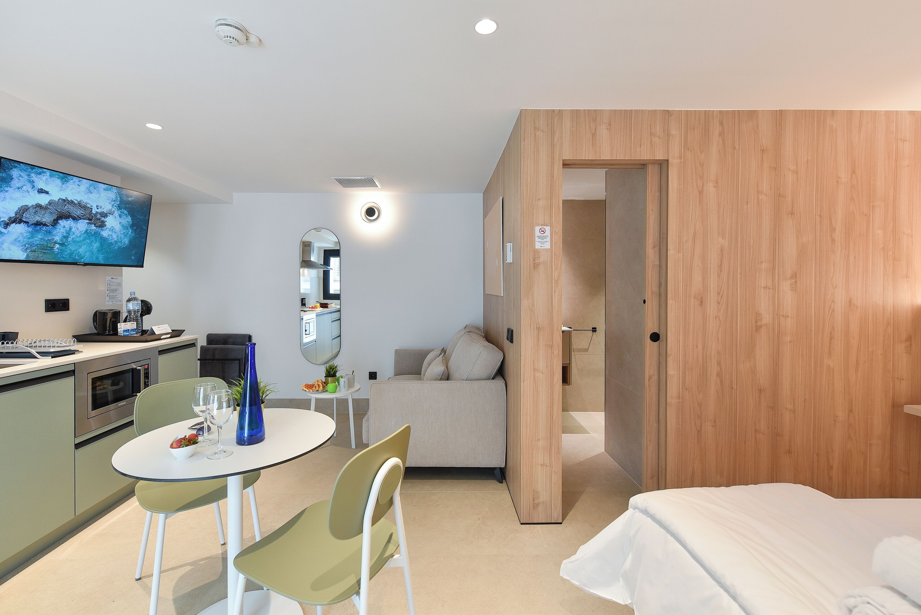 A modern hotel room with a kitchenette, a dining area, a sofa, and a bed.