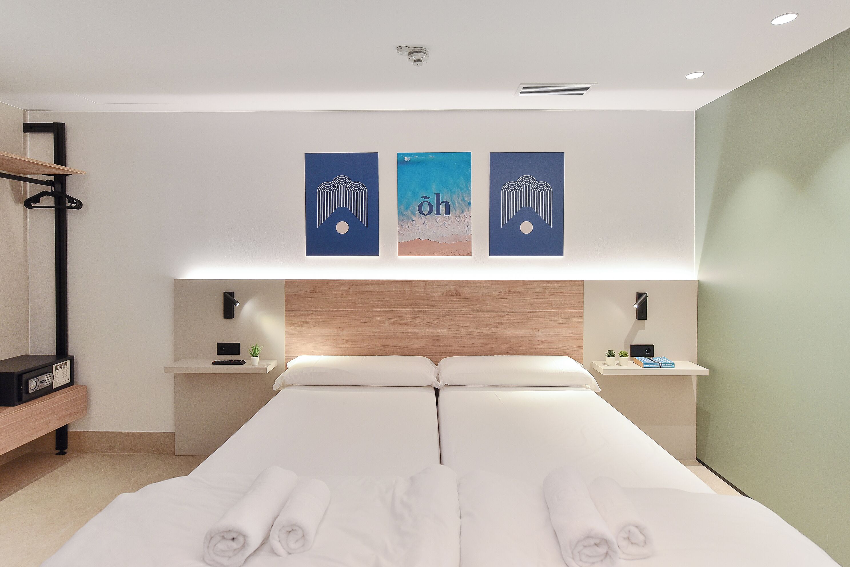 A modern hotel room with a large bed, a wooden headboard, bedside tables with lamps, and artwork on the wall.