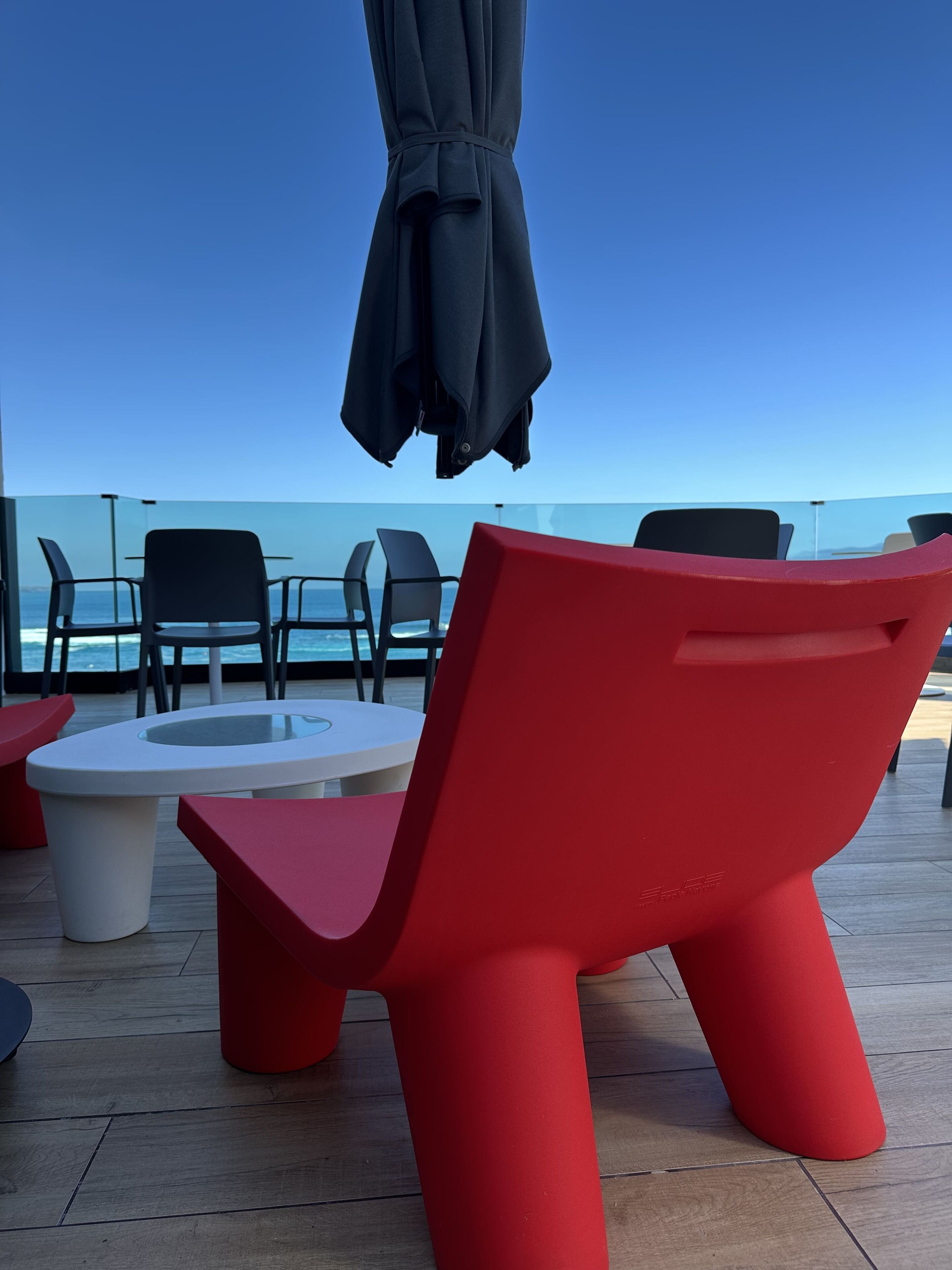 A deck with red and black chairs, a white table, and a black umbrella.