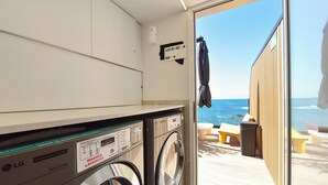 A laundry area with two washing machines, a sign indicating directions to flats and the roof, and a view of the beach through an open door. - OH Suites Paseo de las Canteras 58 (Las Palmas de Gran Canaria)