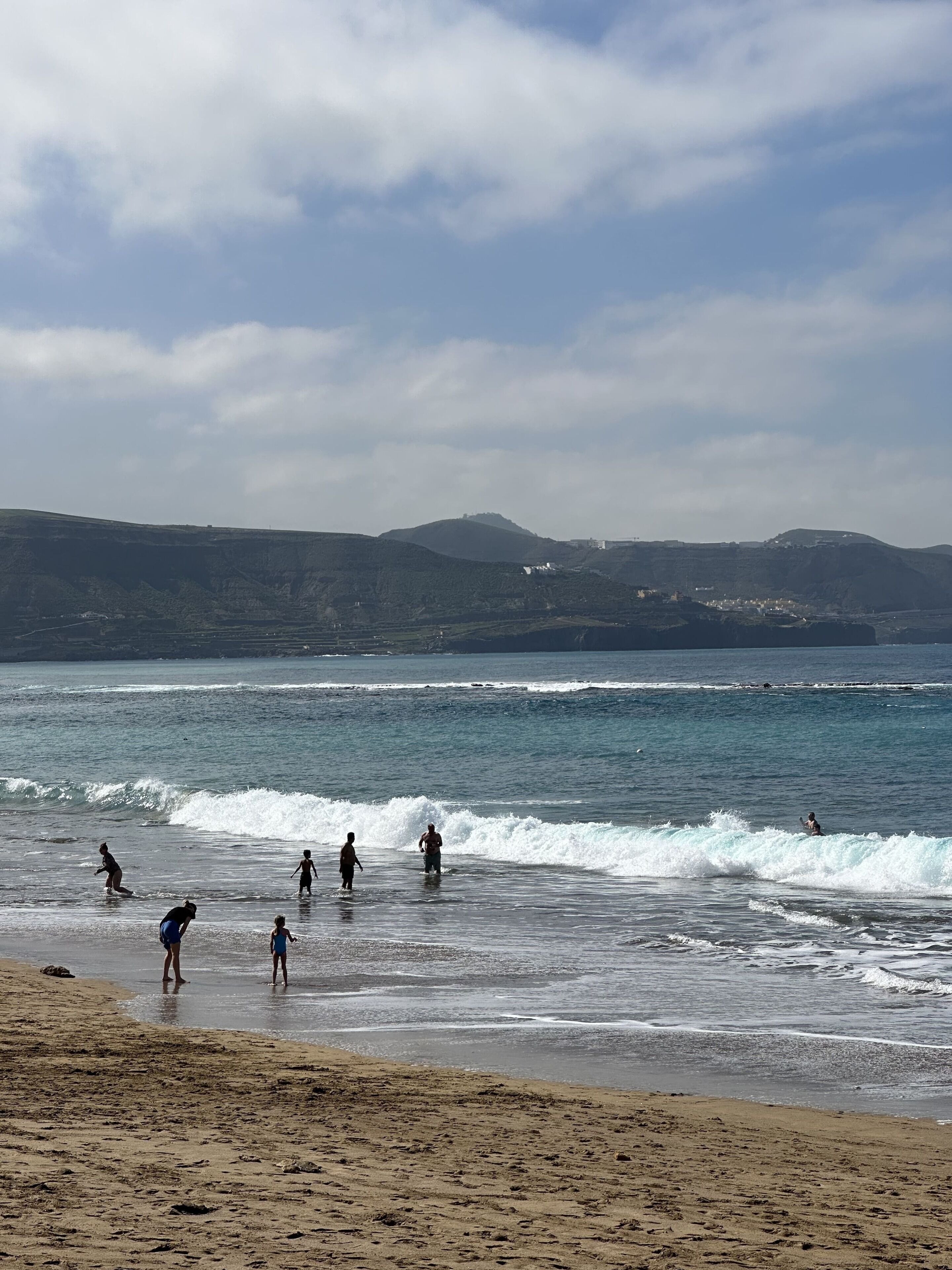 Una spiaggia con persone che giocano in acqua e passeggiano sulla riva.