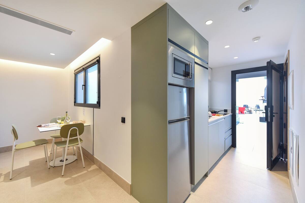 A modern kitchen with a built-in oven and microwave, a dining area with a table and chairs, and a view into the adjacent living space.