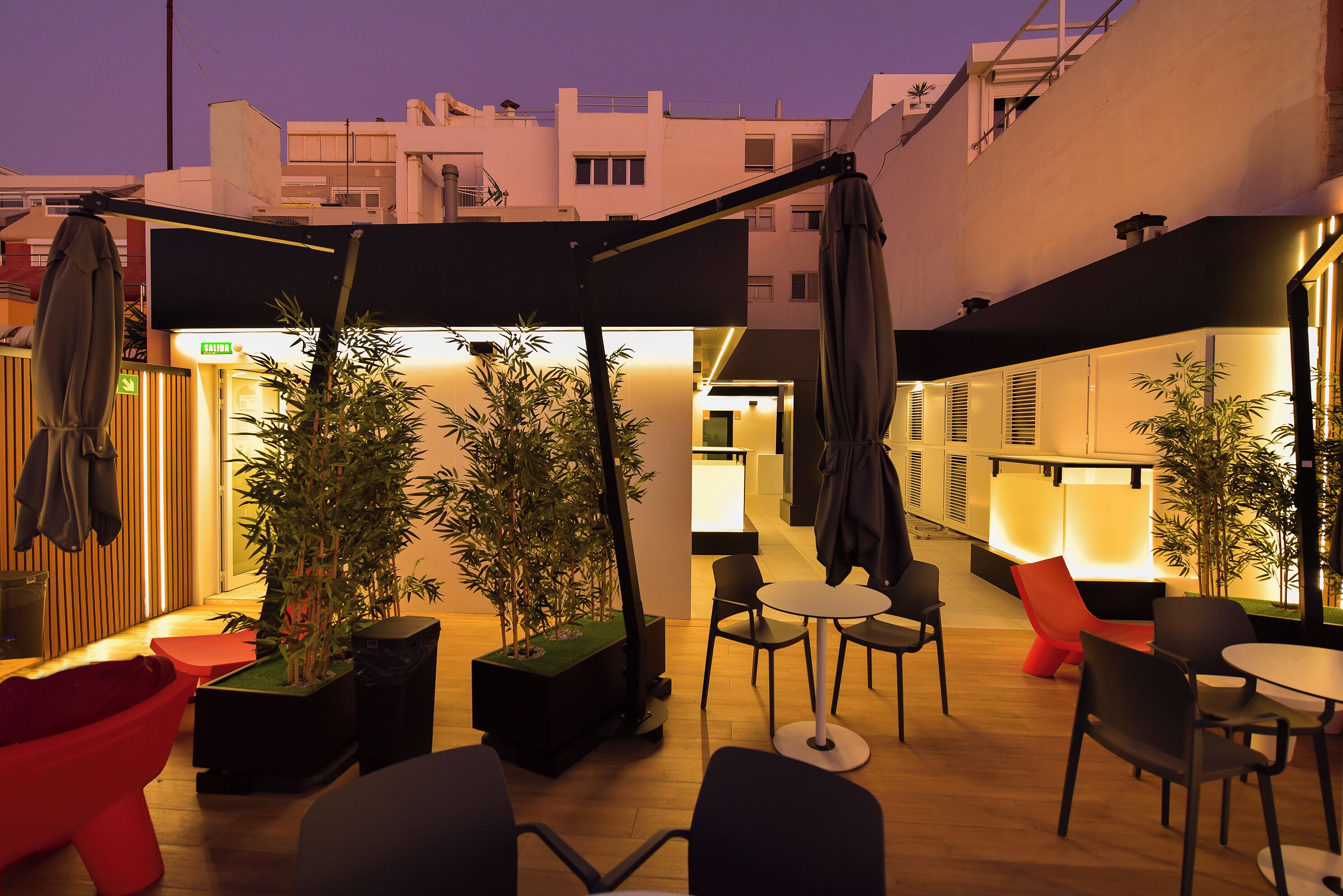 Un espacio al aire libre con mesas, sillas, plantas en macetas y sombrillas.