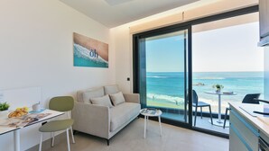 A modern living room with a large window overlooking the ocean, a sofa, a small table, and a desk with a chair. - OH Suites Paseo de las Canteras 58 (Las Palmas de Gran Canaria)