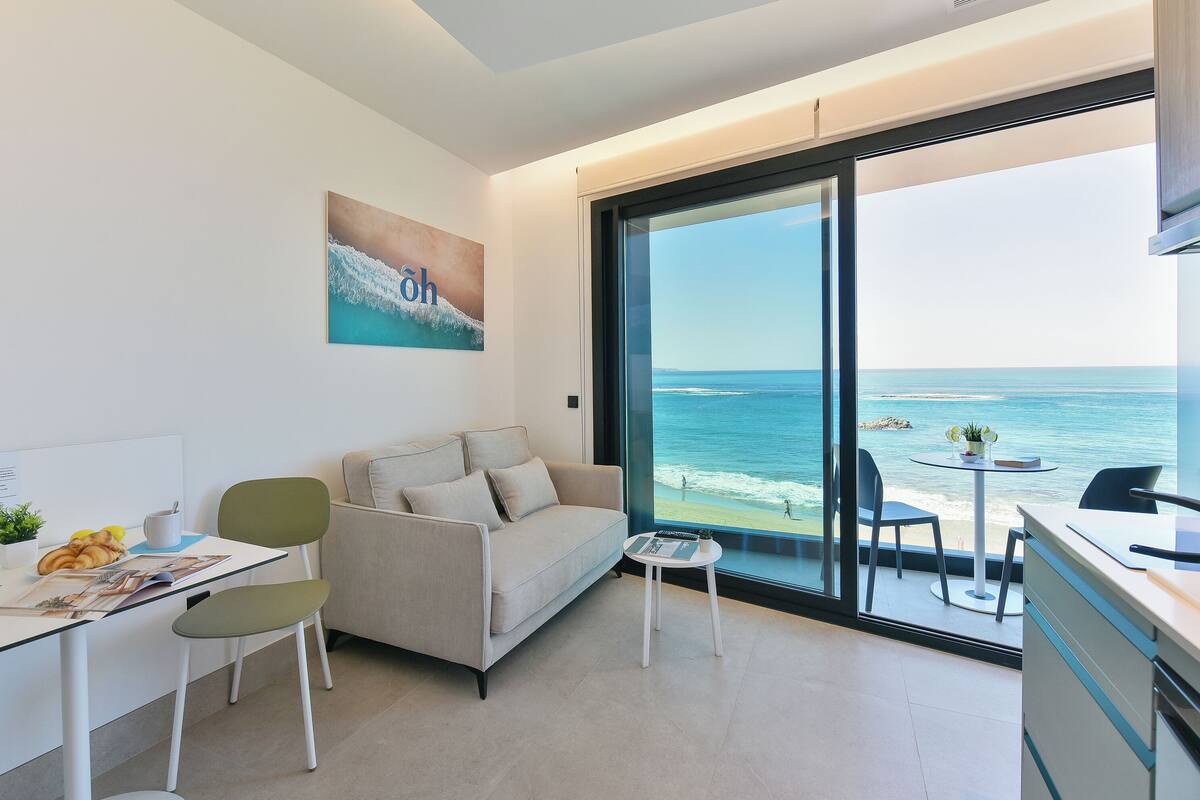 A modern living room with a large window overlooking the ocean, a sofa, a small table, and a desk with a chair.