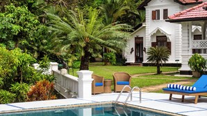 A pool area with lounge chairs, a white building with a red roof, and lush greenery. - Clingendael Weligama (Weligama)