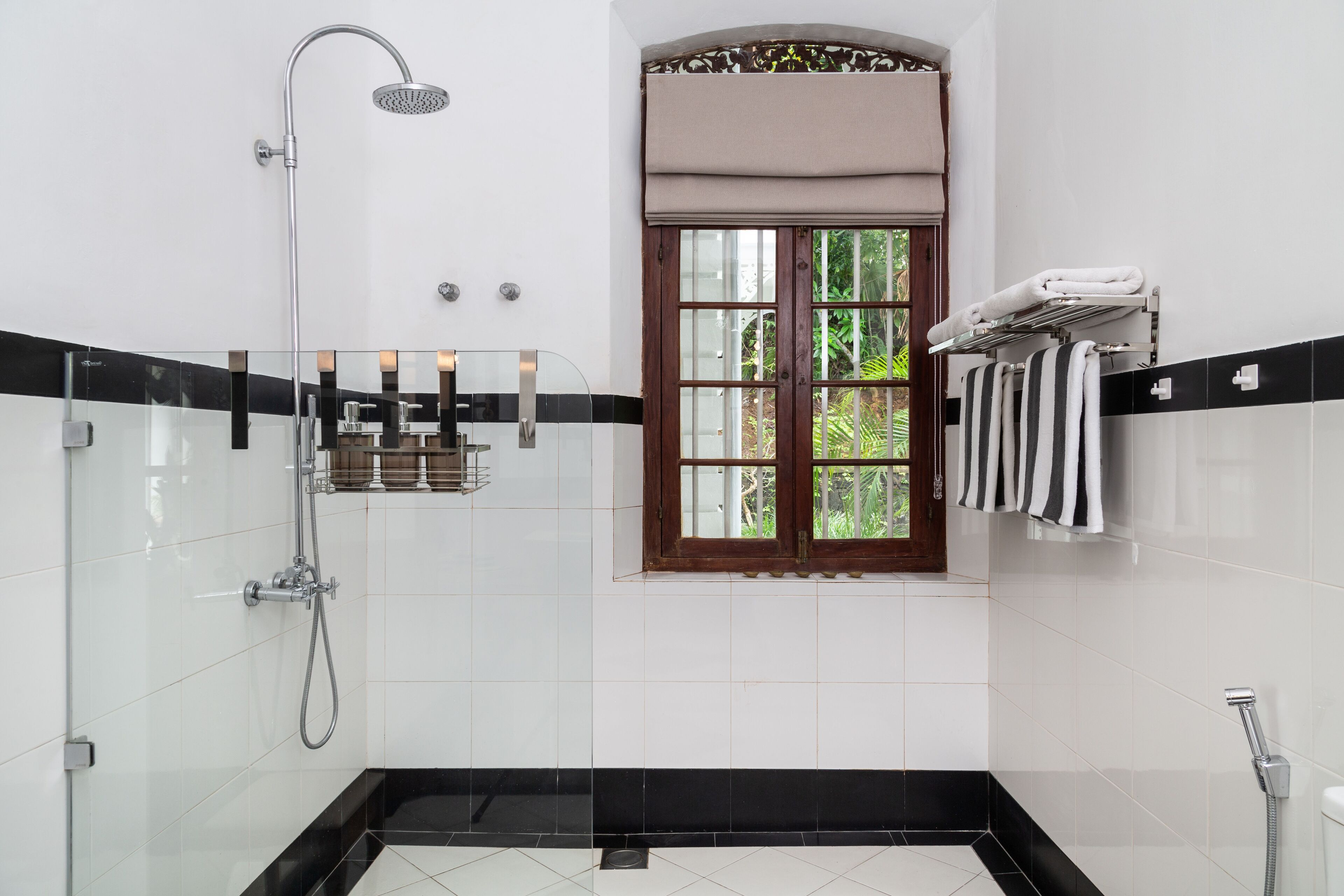 A modern bathroom with a glass shower enclosure, a window with a view of greenery, and a towel rack with striped towels.