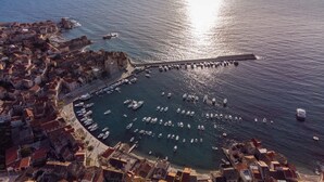 Une vue aérienne d’une ville côtière, avec un port de plaisance rempli de bateaux, une jetée imposante et des bâtiments historiques.