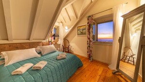 Une chambre à coucher avec un lit, une chaise, une fenêtre donnant sur un beau paysage et un miroir.