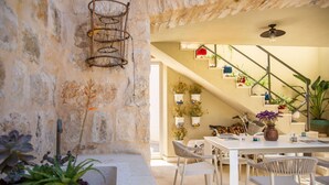 Un mur de pierres apparentes agrémenté d’une étagère en métal, une table blanche avec des chaises et des plantes en pot.