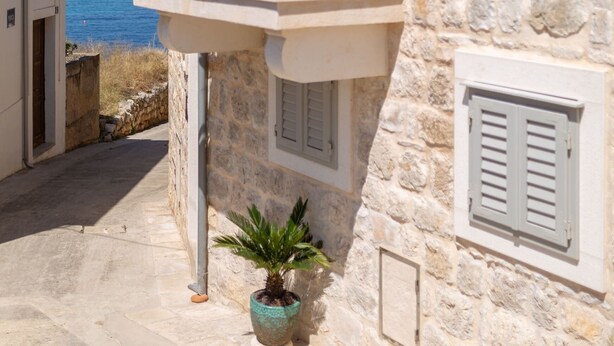 Un bâtiment en pierre doté d’un balcon donnant sur la mer, agrémenté de plantes en pot et de volets.