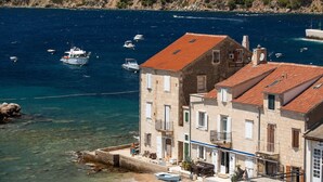 Un bâtiment situé sur la côte, doté d’un toit recouvert de tuiles rouges, d’une façade en pierre et offrant une vue dégagée sur la mer et les bateaux.