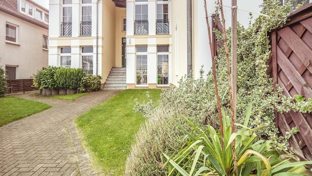 Un immeuble résidentiel à plusieurs étages, doté d’un escalier central, d’un petit jardin à l’avant et d’une clôture en bois.