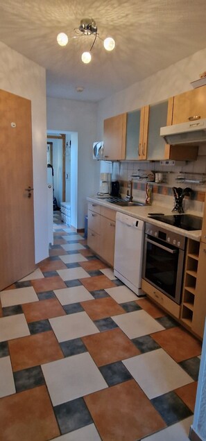 A kitchen with a checkered floor, wooden cabinets, a white dishwasher, and a stove. - Cozy apartment with terrace in Zinnowitz on the island of Usedom (Zinnowitz)