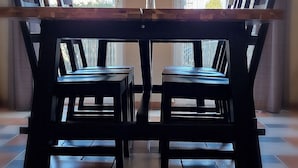 Un espace repas comprenant une table et des chaises en bois, un luminaire suspendu et de grandes fenêtres avec des rideaux.