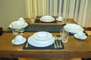 Une table à manger dressée avec de l’assiette blanche, des bols et des couverts, des verres et un set de table.