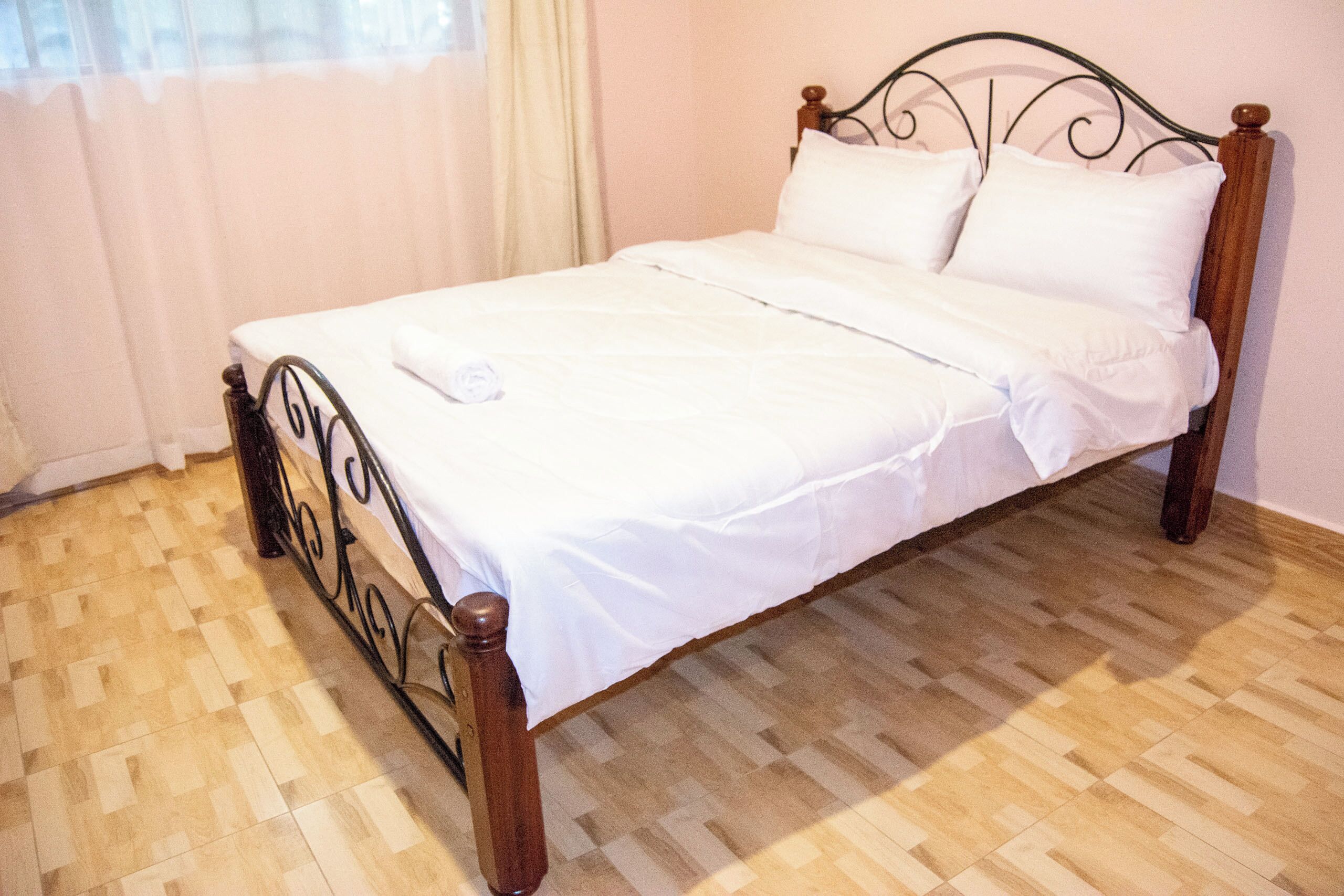 A neatly made bed with white linens and a wooden headboard in a room with a herringbone-patterned wooden floor.