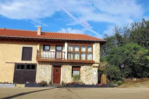 A two-story stone building with a red-tiled roof, a wooden balcony, and a small garden area. - Find the north in the "House of the good way". (Oreña)