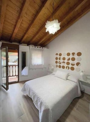 A bedroom with a wooden ceiling, a bed with white bedding, a circular wall decoration, and a window with curtains. - Find the north in the "House of the good way". (Oreña)