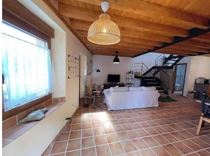 A spacious living area with a sofa, a TV, a staircase, and a large window. - Find the north in the "House of the good way". (Oreña)