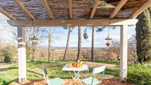 En uteplats med ett bord och stolar, en pergola ovanför och en utsikt över träd och kullar i bakgrunden.